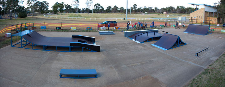 Regional skatepark with blue steel ramps and a concrete pad beside a sports field