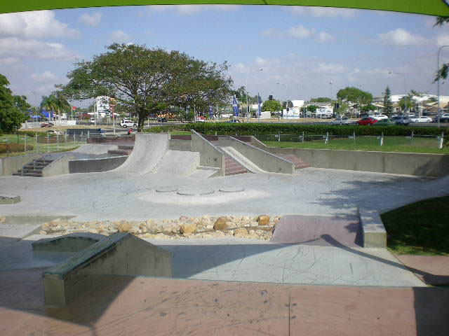 Concrete skatepark with banks, stairs and a rock feature beside a suburban road