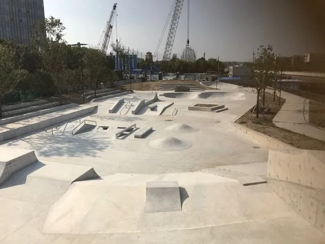 Concrete skatepark plaza under construction with cranes in the background