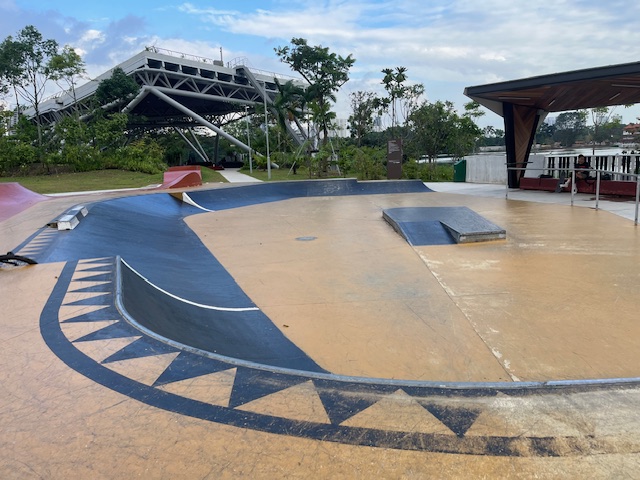 Singapore beginner-friendly skatepark plaza with flowing concrete banks, ramps and decorative markings near a sheltered pavilion
