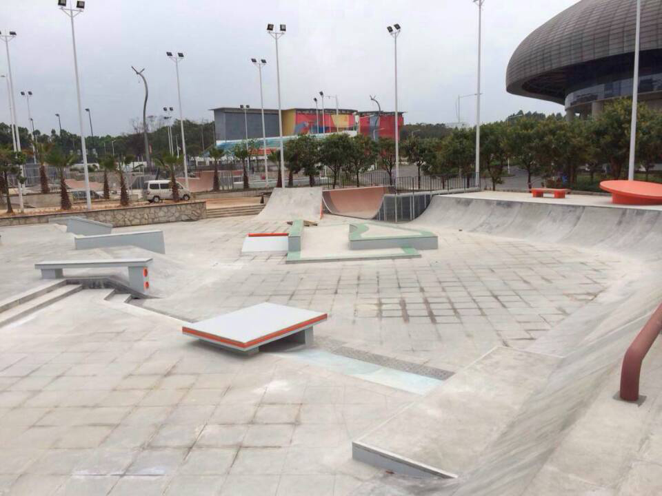 Concrete skate plaza with ledges, rails and a modern arena in the background at Guangzhou University City Mega Skatepark