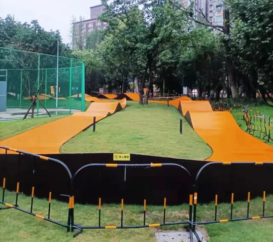 Orange asphalt pump track winding through a treed park