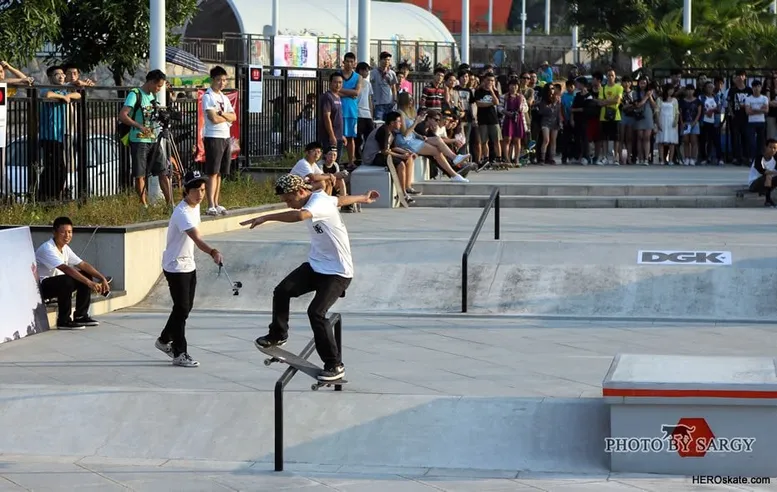 Skateboarder grinding a rail in a concrete plaza during a competition with a large crowd watching