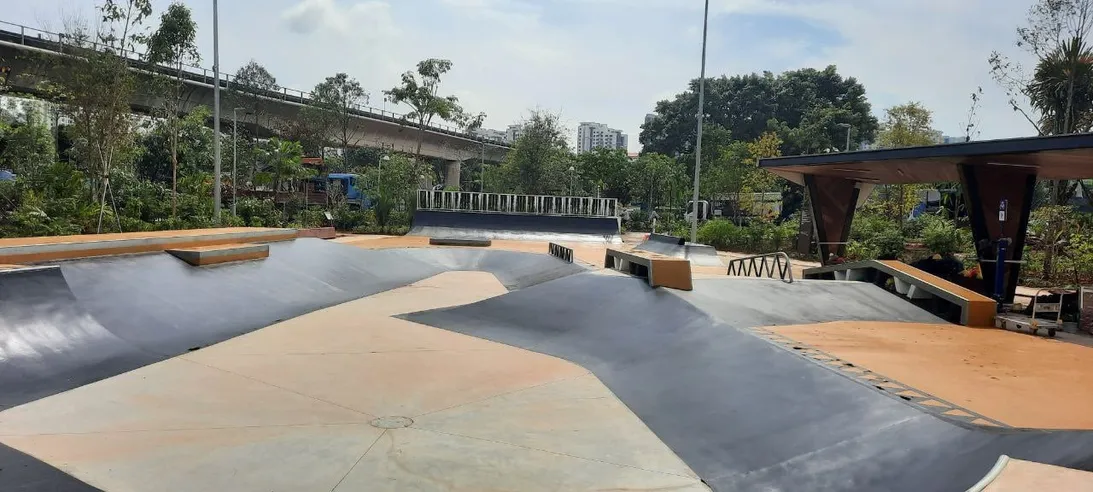 Modern concrete skatepark with flowing banks beside an elevated rail line
