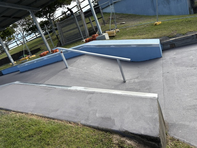 Completed concrete skatepark repairs with blue painted ramps and steel rail
